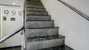 A staircase with granite steps and a metal handrail, leading to a landing with clocks and signs indicating time zones. - FabExpress Golden Sands inn (Mumbai)