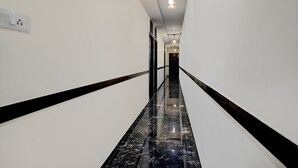 A hallway with white walls, black marble flooring, and a black handrail. - FabExpress Golden Sands inn (Mumbai)