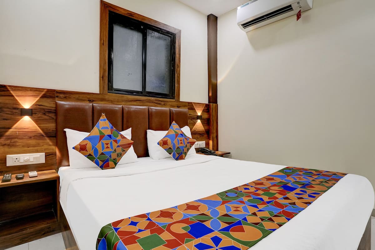 Una cama bien tendida con una colcha de diseño geométrico y colores vivos, un cabecero de madera y una mesita de noche con un teléfono y control remoto.