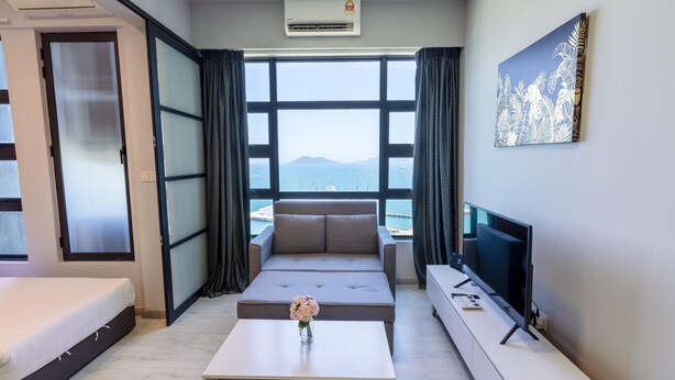 A modern hotel room with a bed, sofa, TV, and a view of the sea. - Capital O 90998 Margo Home (Kota Kinabalu)
