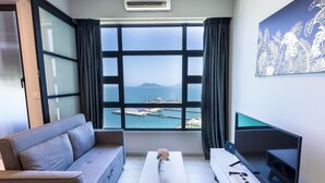 A modern room with a sofa, a coffee table, a TV, and a large window offering a view of a harbor. - Capital O 90998 Margo Home (Kota Kinabalu)