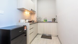 A compact kitchen with a refrigerator, a coffee maker, and a kettle on the counter. - Capital O 90998 Margo Home (Kota Kinabalu)