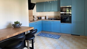 Uma cozinha moderna com armários verde-água, bancada de madeira, lustre e área de jantar com mesa e cadeiras.