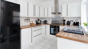 Eine moderne Küche mit weißen Schränken, einem schwarzen Kühlschrank, einem eingebauten Backofen und einem Geschirrgestell.