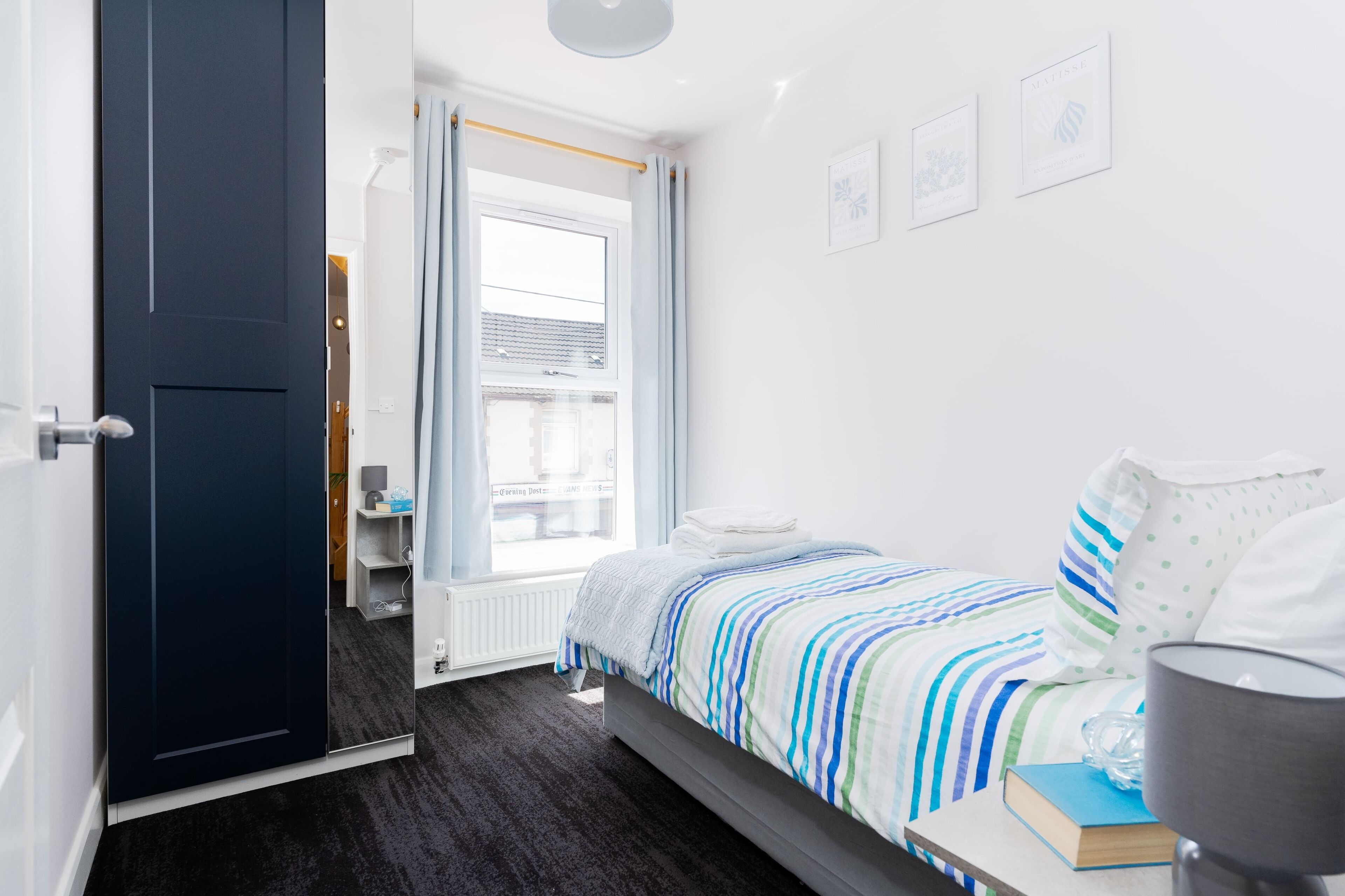 A modern bedroom with a bed, a bedside table, a lamp, and a window.