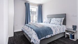 Ein Schlafzimmer mit einem Bett, einem Nachttisch, einem Fenster mit Vorhängen und einem Kopfteil.