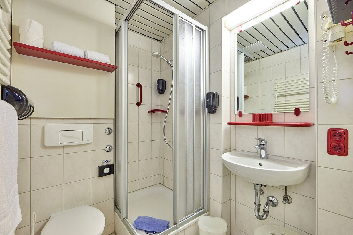 Een badkamer met douche, toilet, wastafel en spiegel.