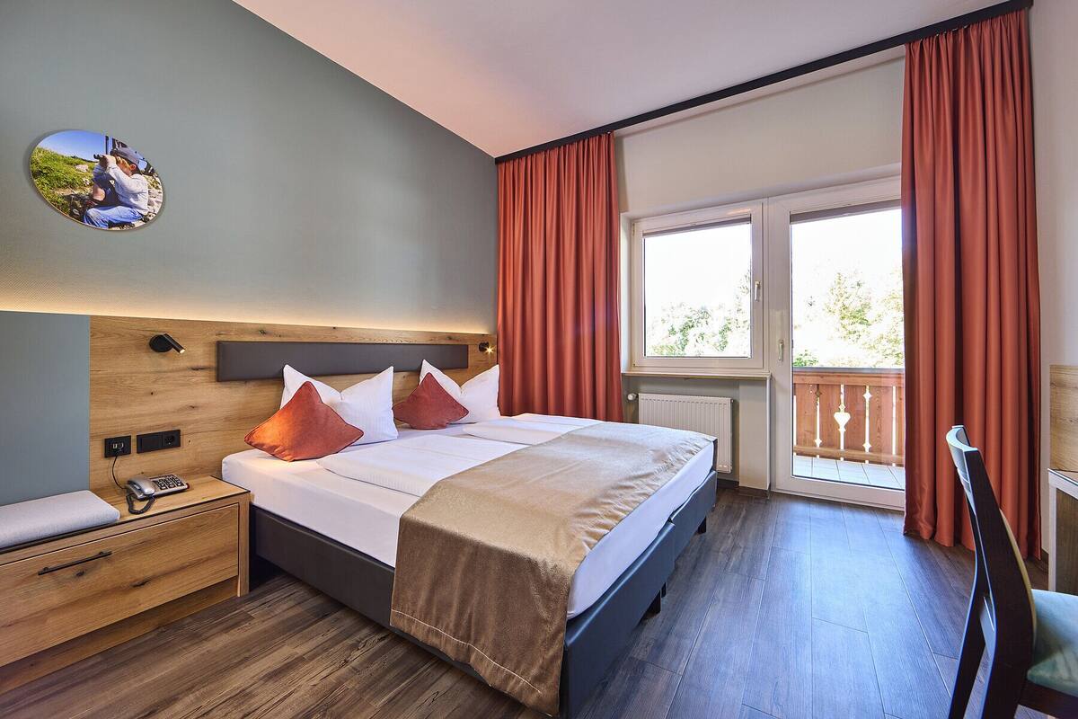 Een hotelkamer met een bed, nachtkastje, lamp en uitzicht op het landschap.
