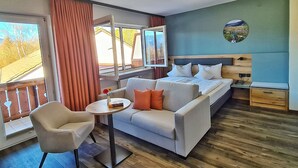 A room with a bed, a sofa, a chair, a small table, and a window with curtains. - Aura Hotel Saulgrub (Saulgrub)