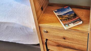 A bed with pillows, a wooden nightstand with a book, and a drawer with a pen.