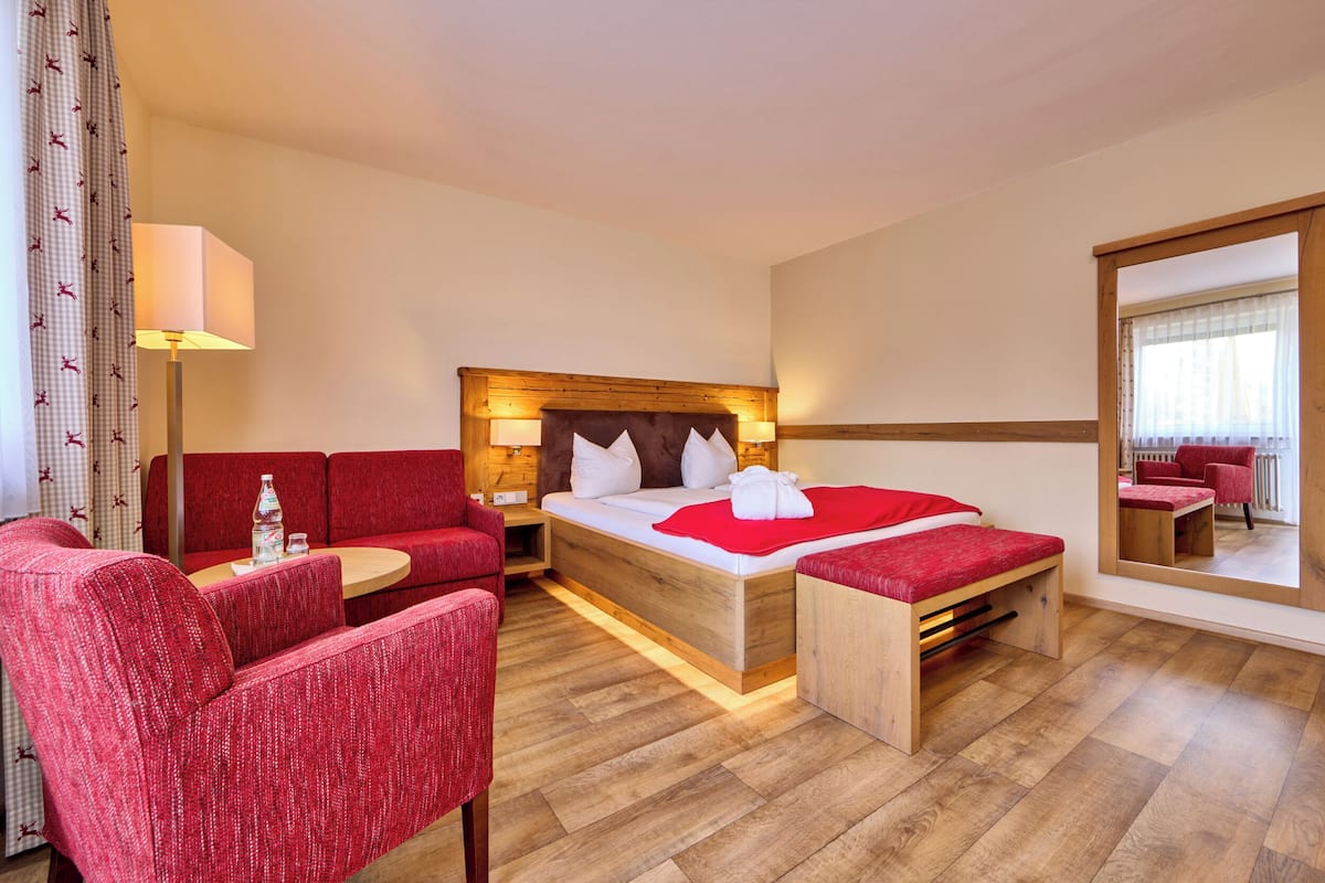 Een hotelkamer met een bed, een zithoek met rode fauteuils, een tafeltje en een spiegel aan de muur.