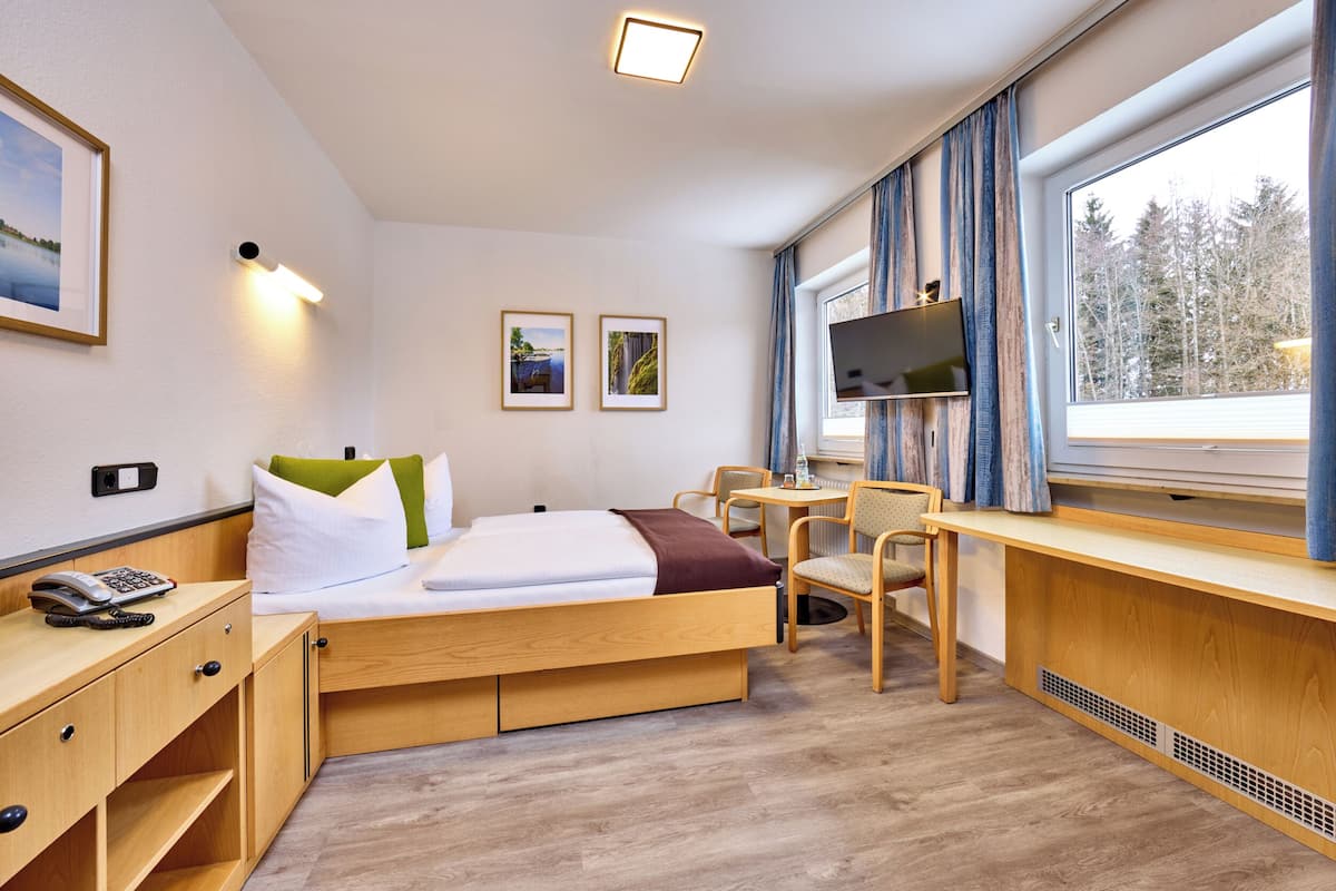 Een moderne hotelkamer met een bed, bureau, stoel en groot raam.