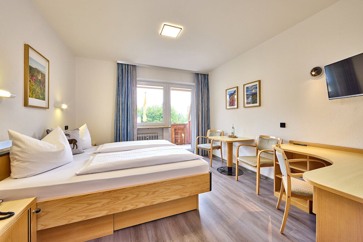 Een hotelkamer met een bed, een bureau, twee stoelen, een televisie en een raam met gordijnen.