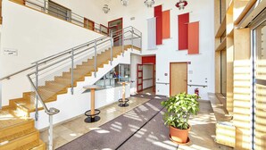 A spacious lobby with a wooden staircase, a reception desk, and a potted plant. - Aura Hotel Saulgrub (Saulgrub)