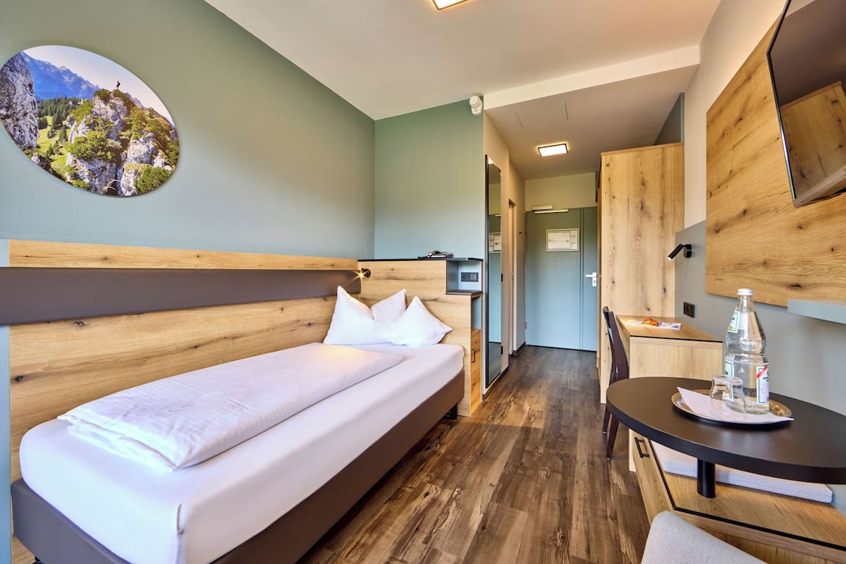 Een moderne hotelkamer met een houten bed, een eettafel met een fles en glazen, en uitzicht op een bergachtig landschap.