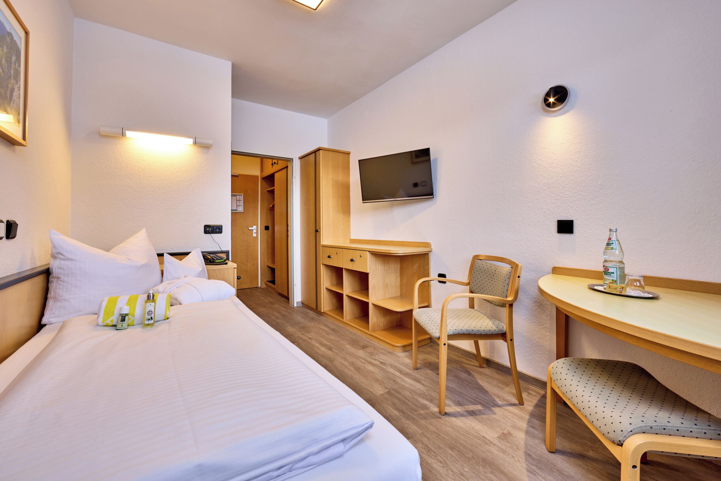 Une chambre d’hôtel comprenant un lit, un bureau avec une chaise, un téléviseur fixé au mur et une armoire en bois.