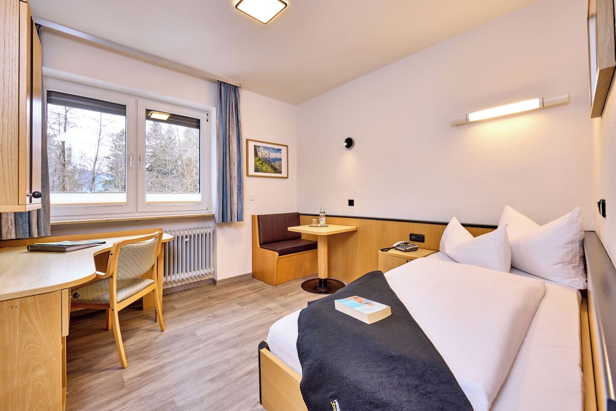 Een hotelkamer met een bed, een bureau, een stoel, een klein tafeltje en een raam met gordijnen.