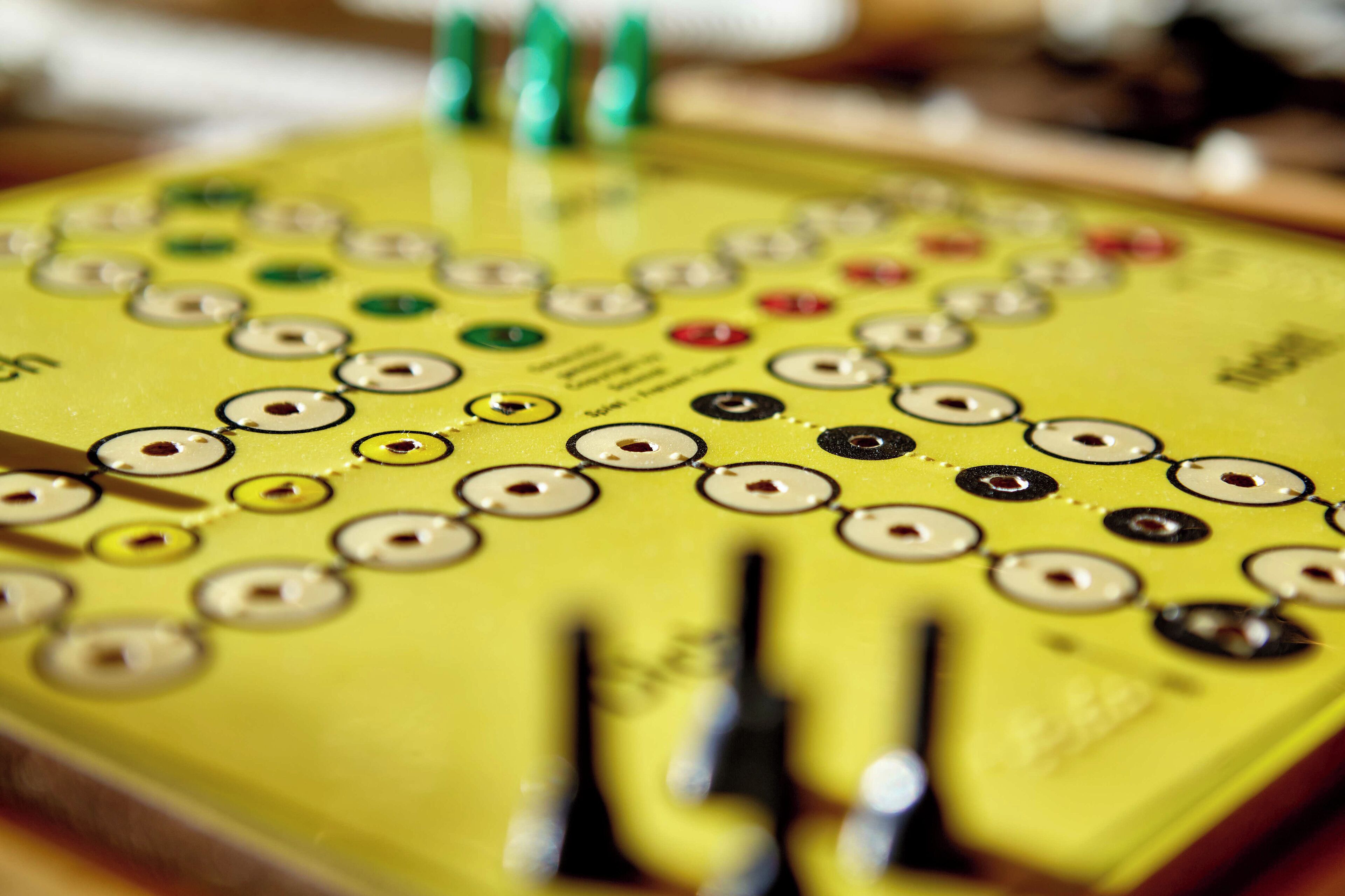 A close-up of a yellow board with circular buttons and green pins, likely part of a game or control panel.