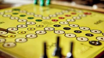 A close-up of a yellow board with circular buttons and green pins, likely part of a game or control panel.