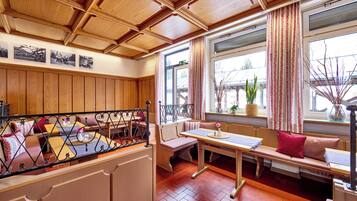 A cozy room with wooden paneling, a bench with cushions, a table, and a window with curtains.