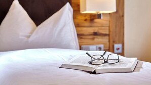 A neatly made bed with white linens, a pair of glasses, and an open book on it. - Aura Hotel Saulgrub (Saulgrub)