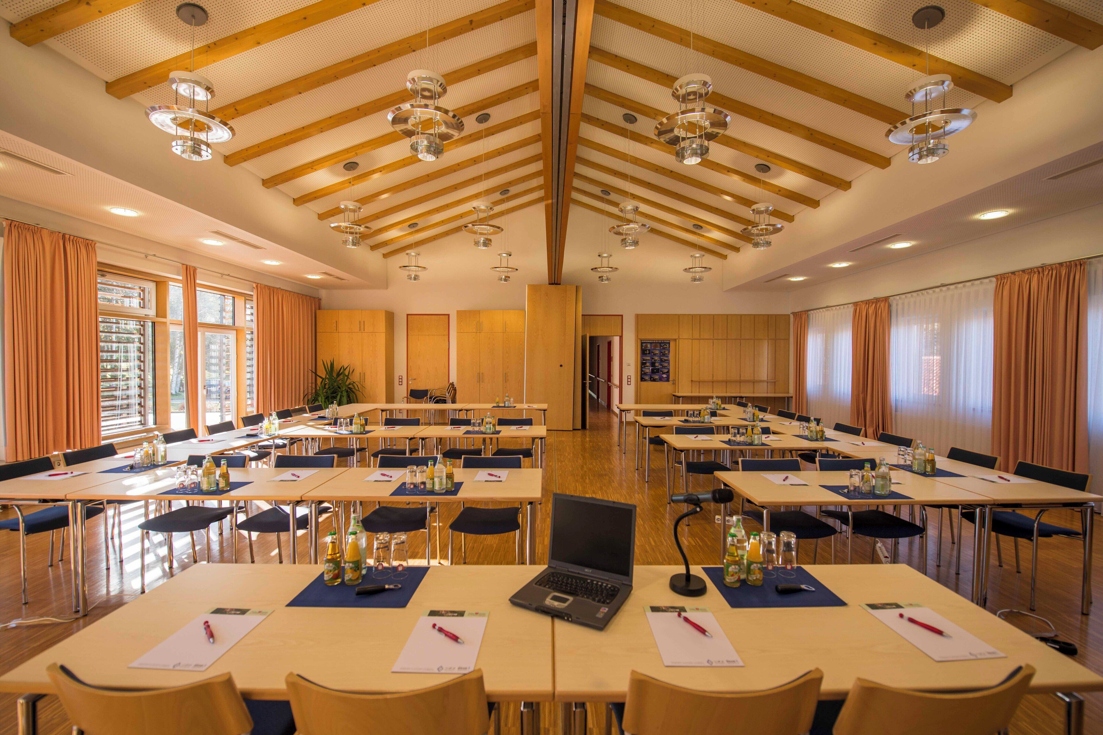 A conference room with multiple tables, chairs, and a laptop on one table.