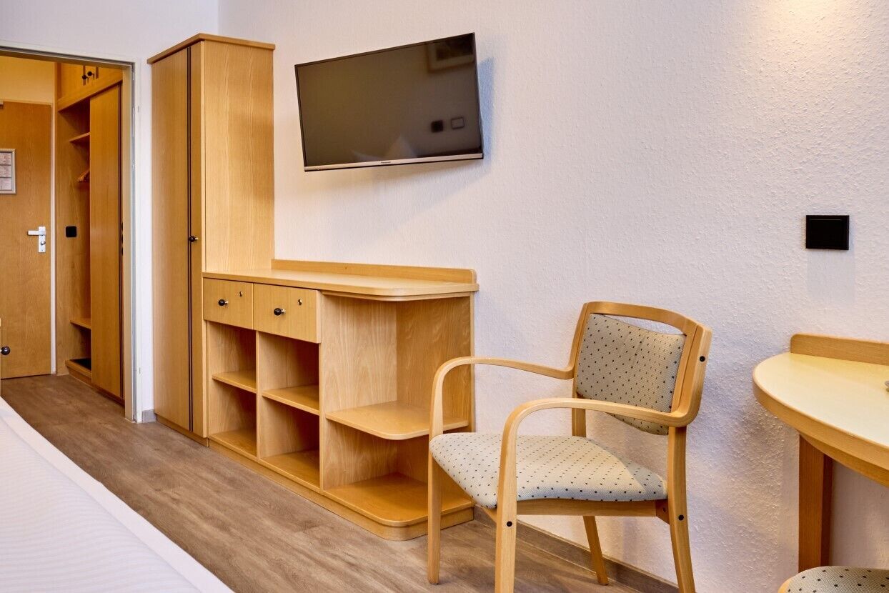A room with a wooden cabinet, a television mounted on the wall, a chair, and a small table.