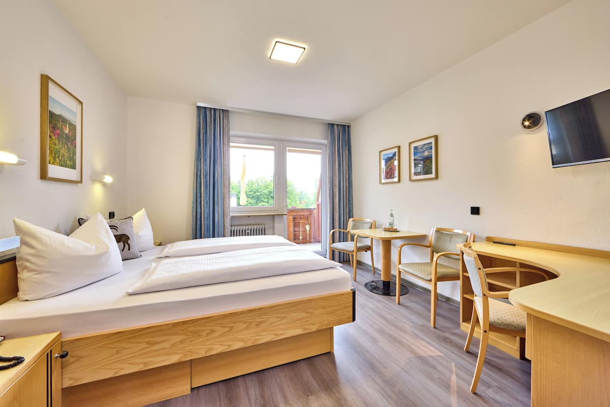 Een hotelkamer met een bed, bureau, stoelen, televisie en een raam met gordijnen.