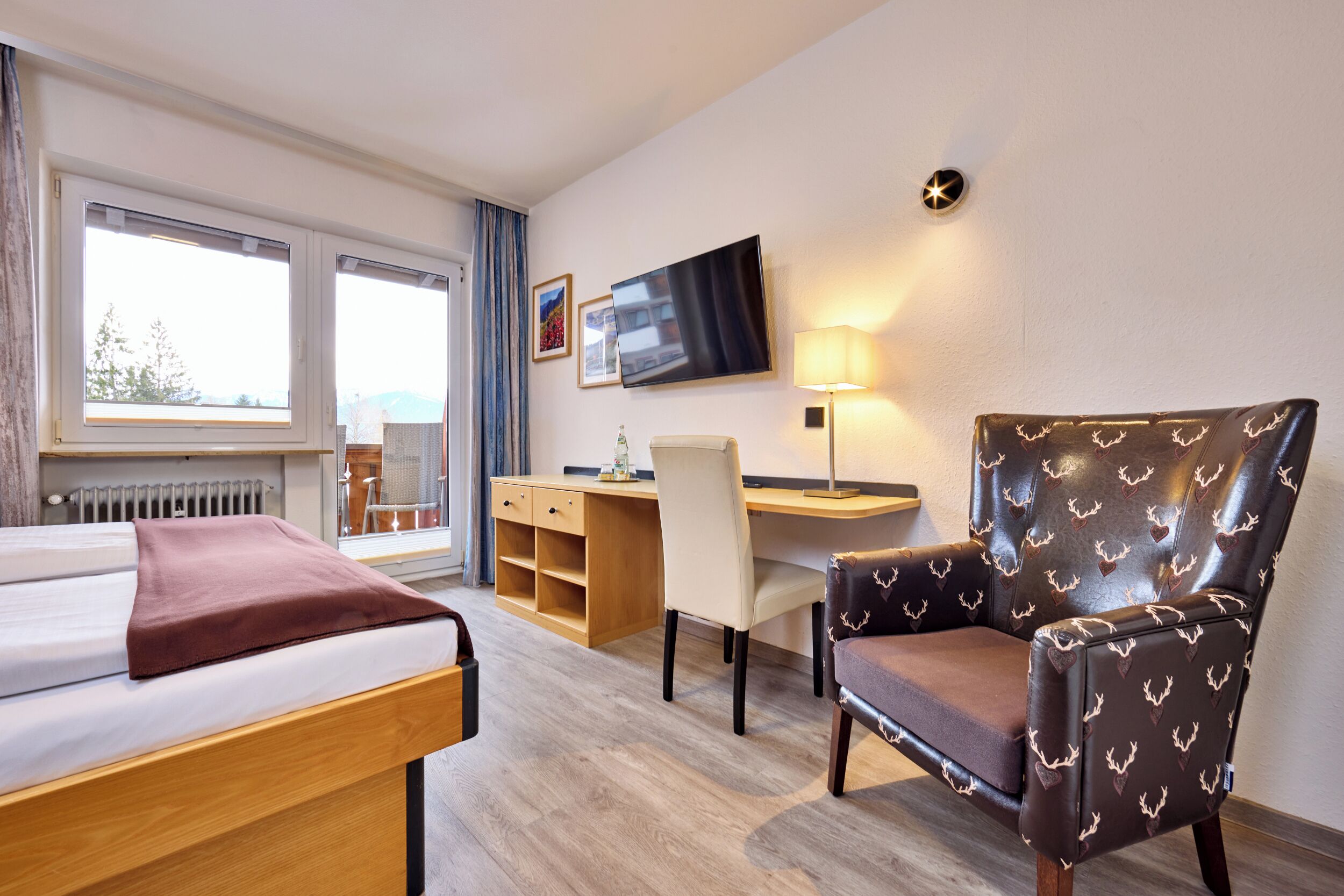 Ein Hotelzimmer mit Bett, Schreibtisch, Sessel, Fernseher und einem Fenster mit Vorhängen.