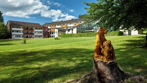 A building with multiple balconies and a grassy area with a wooden sculpture. - Aura Hotel Saulgrub (Saulgrub)