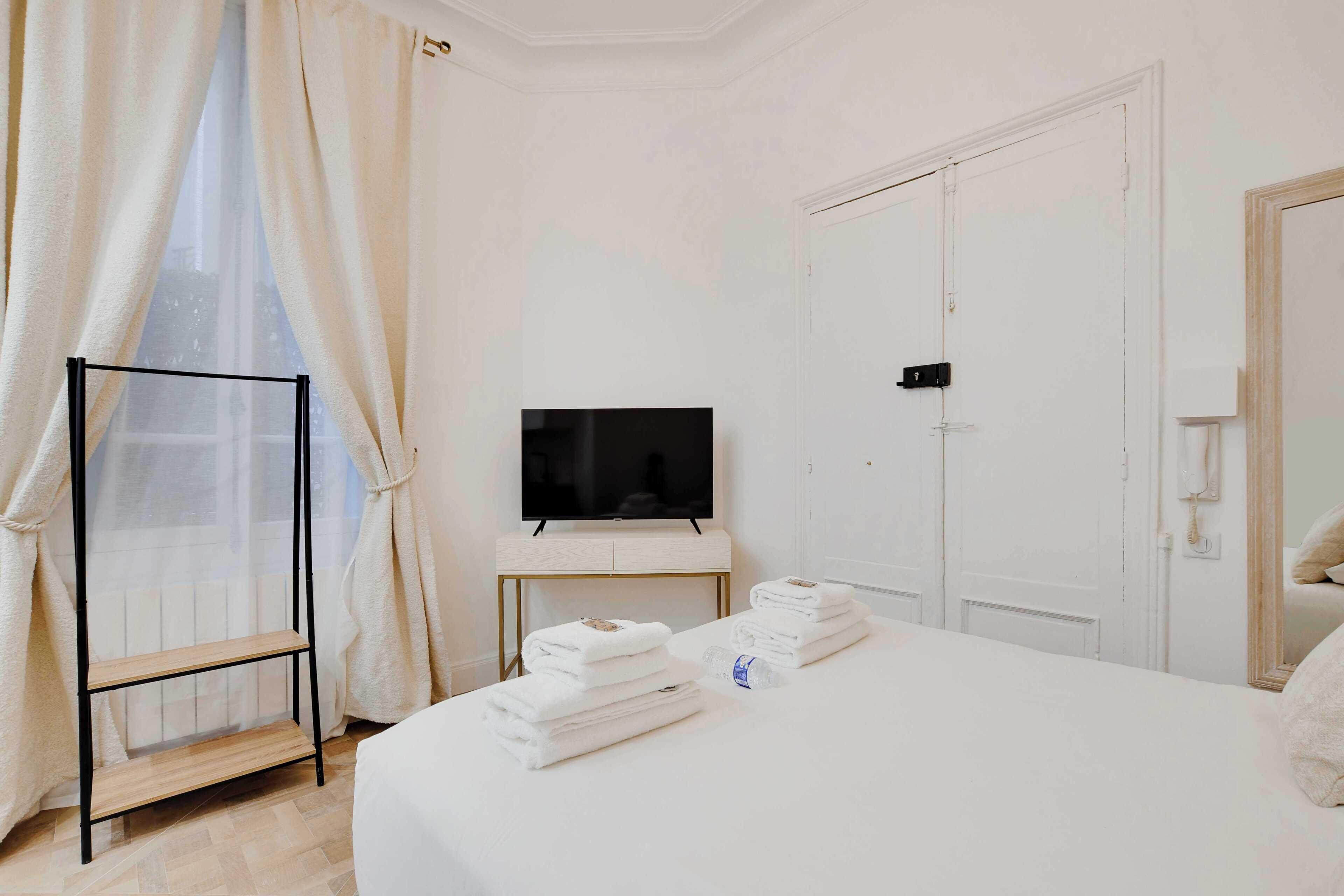 Une chambre d’hôtel équipée d’un lit, d’une télévision, d’une armoire et d’une étagère avec des serviettes.
