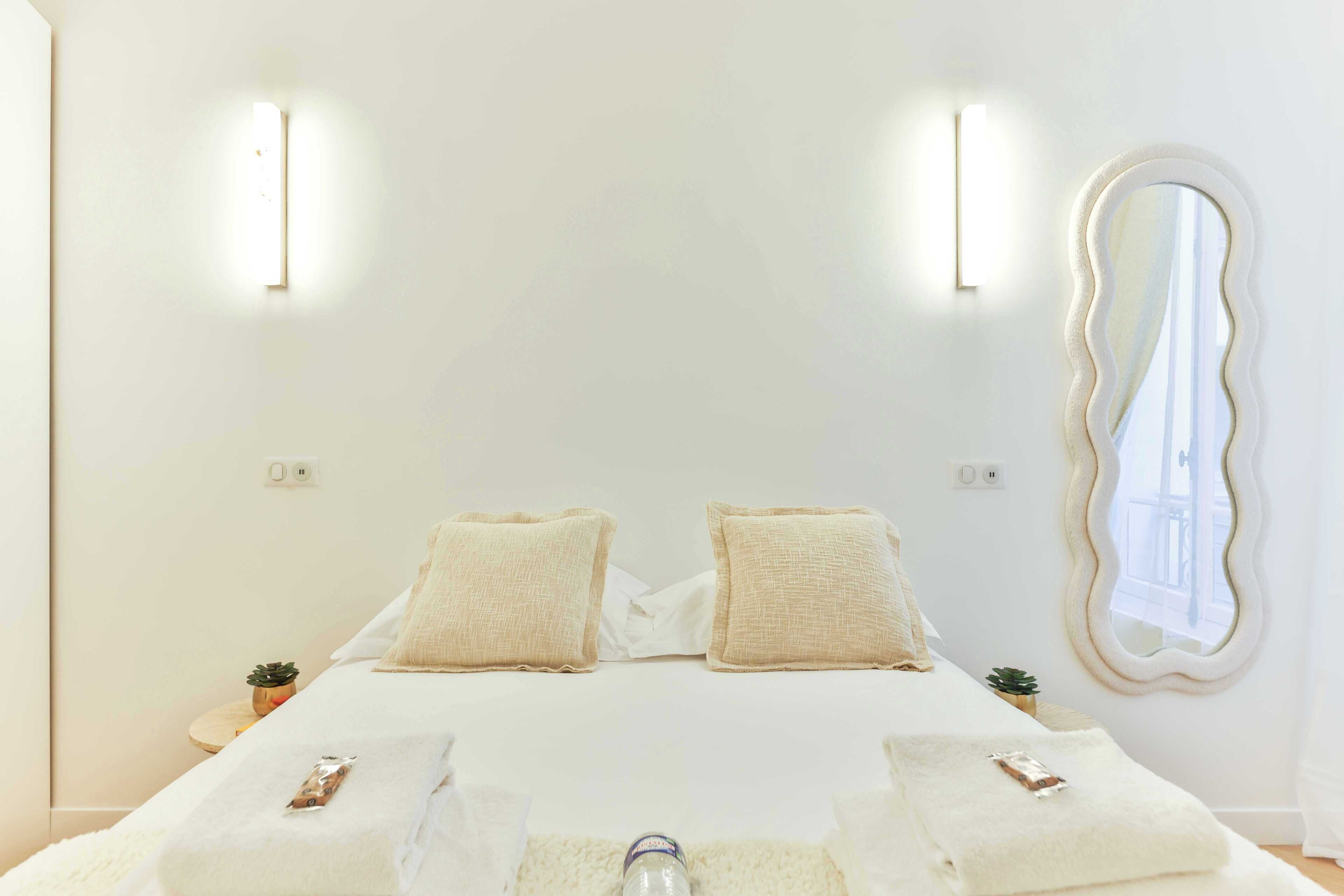 Una camera da letto minimalista con un letto, due comodini, uno specchio e luci a parete.