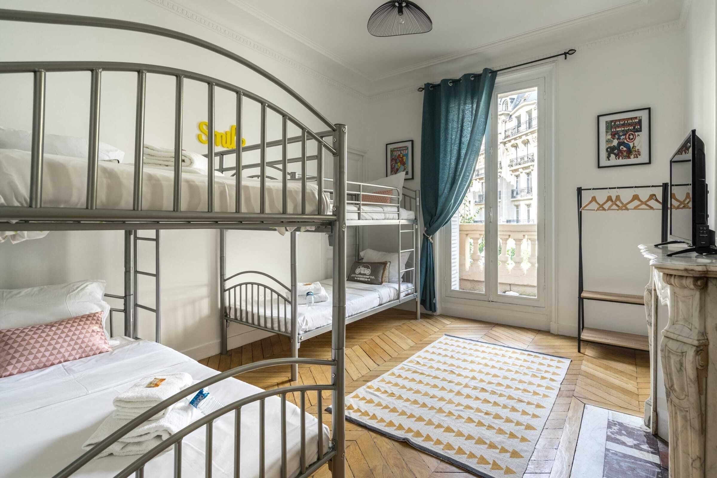 A room with bunk beds, a window with curtains, a hanging rack, and a mirror.