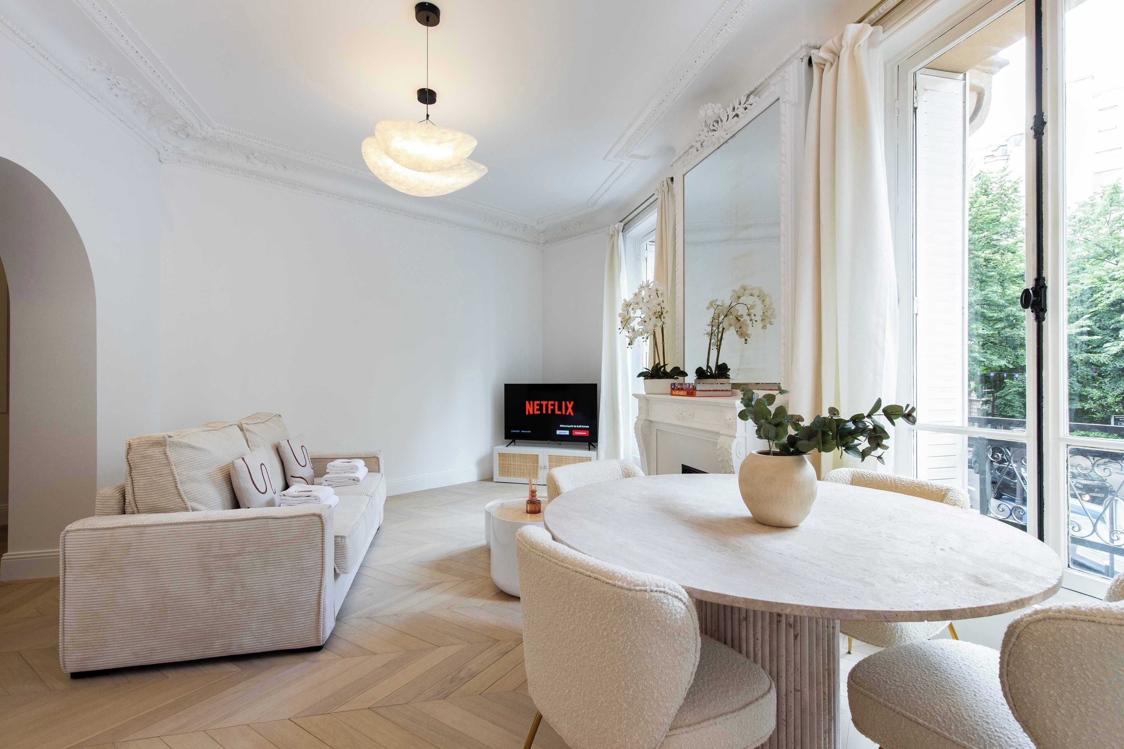 A modern living room with a sofa, a round dining table, and a TV displaying 'NETFLIX'.