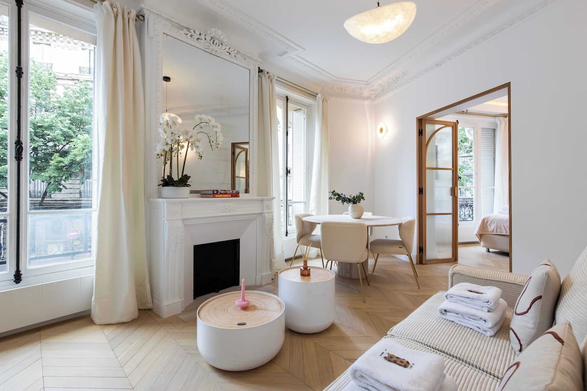 A spacious living room with a fireplace, round tables, and a sofa with towels.