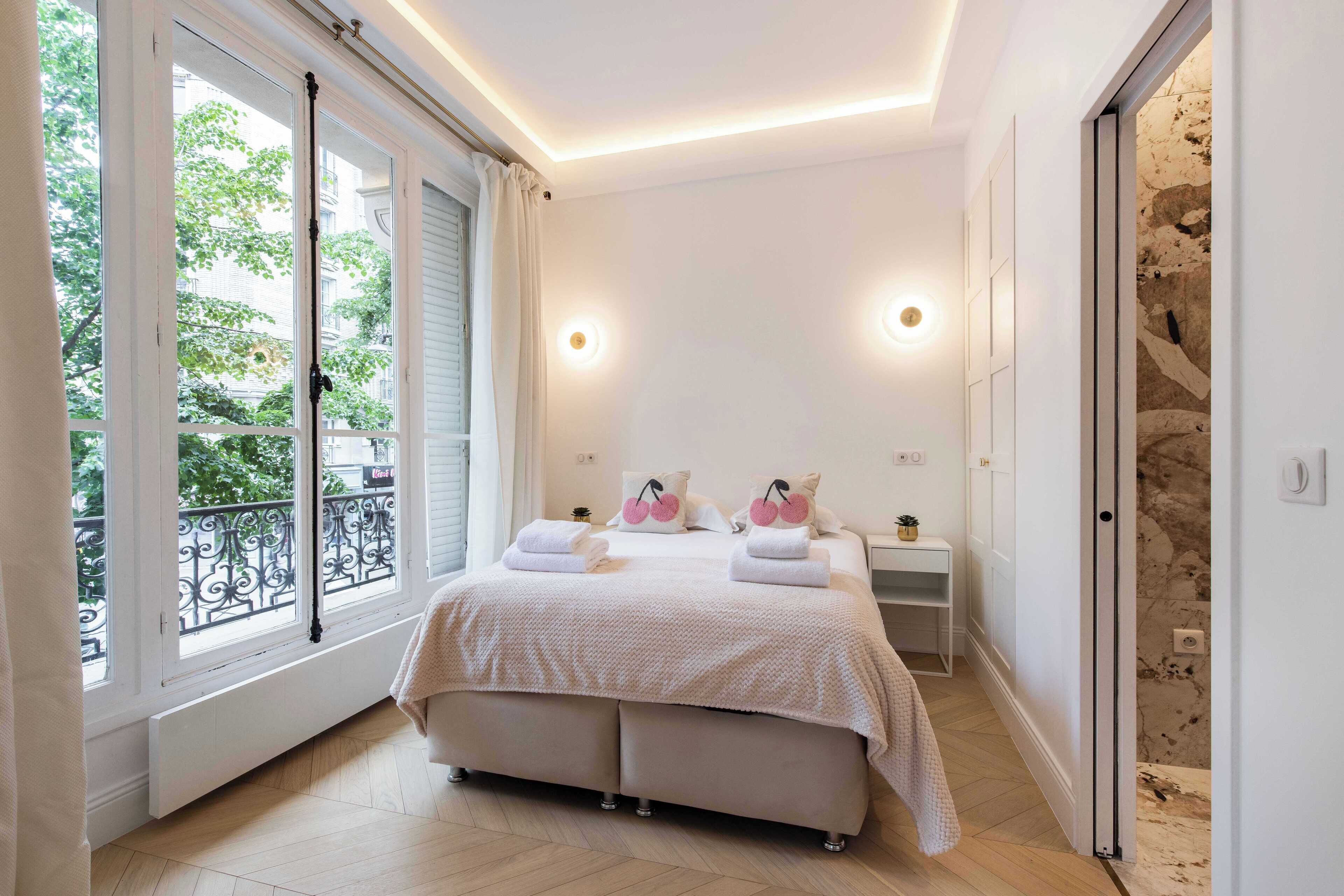 Une chambre dotée d’un grand lit, de deux tables de chevet, d’une fenêtre donnant sur un paysage verdoyant et d’une porte menant à un balcon.