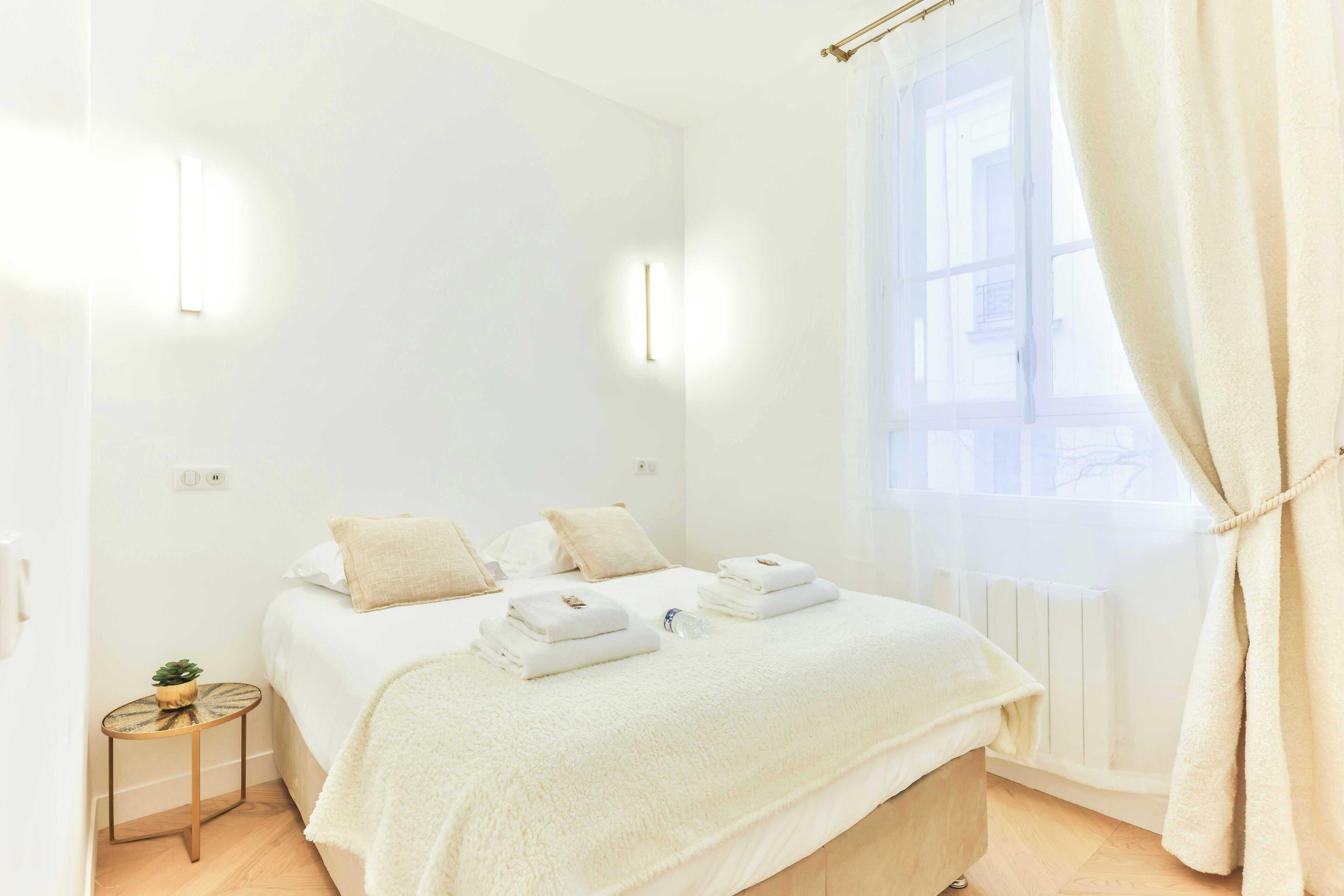 A modern bedroom with a large bed, bedside tables, and a window with curtains.