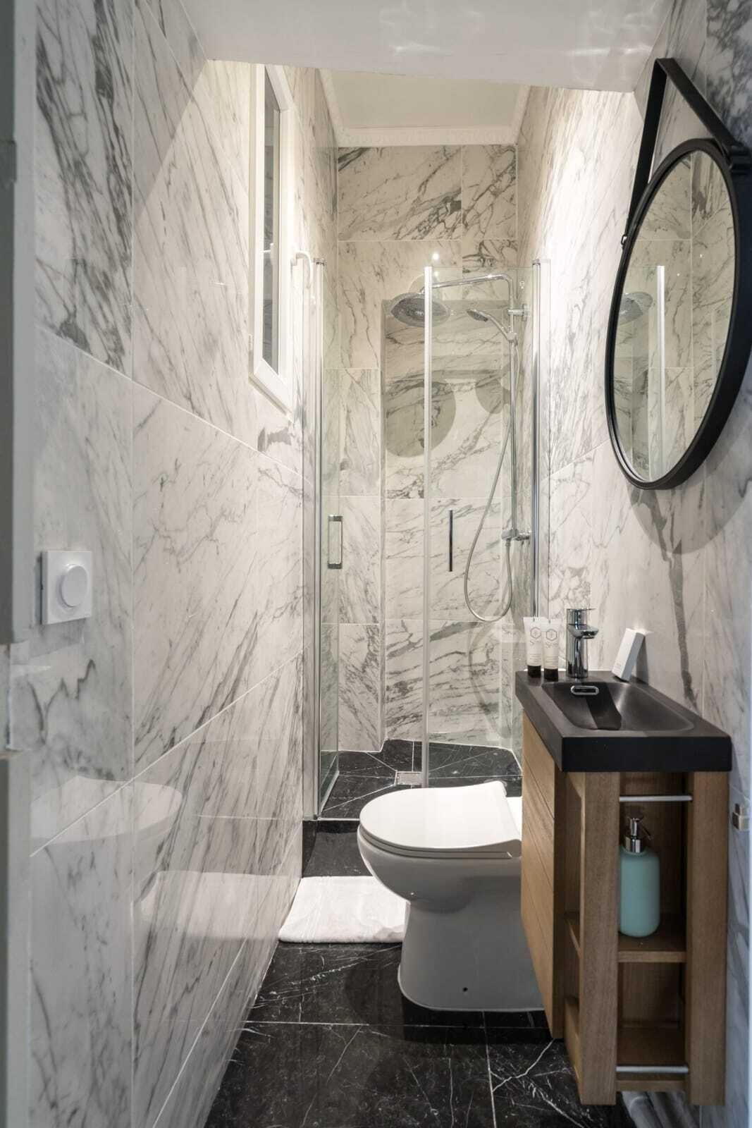 Ein Badezimmer mit Marmorwänden, einer gläsernen Dusche, einer Toilette und einem Holzausleger mit Waschbecken.