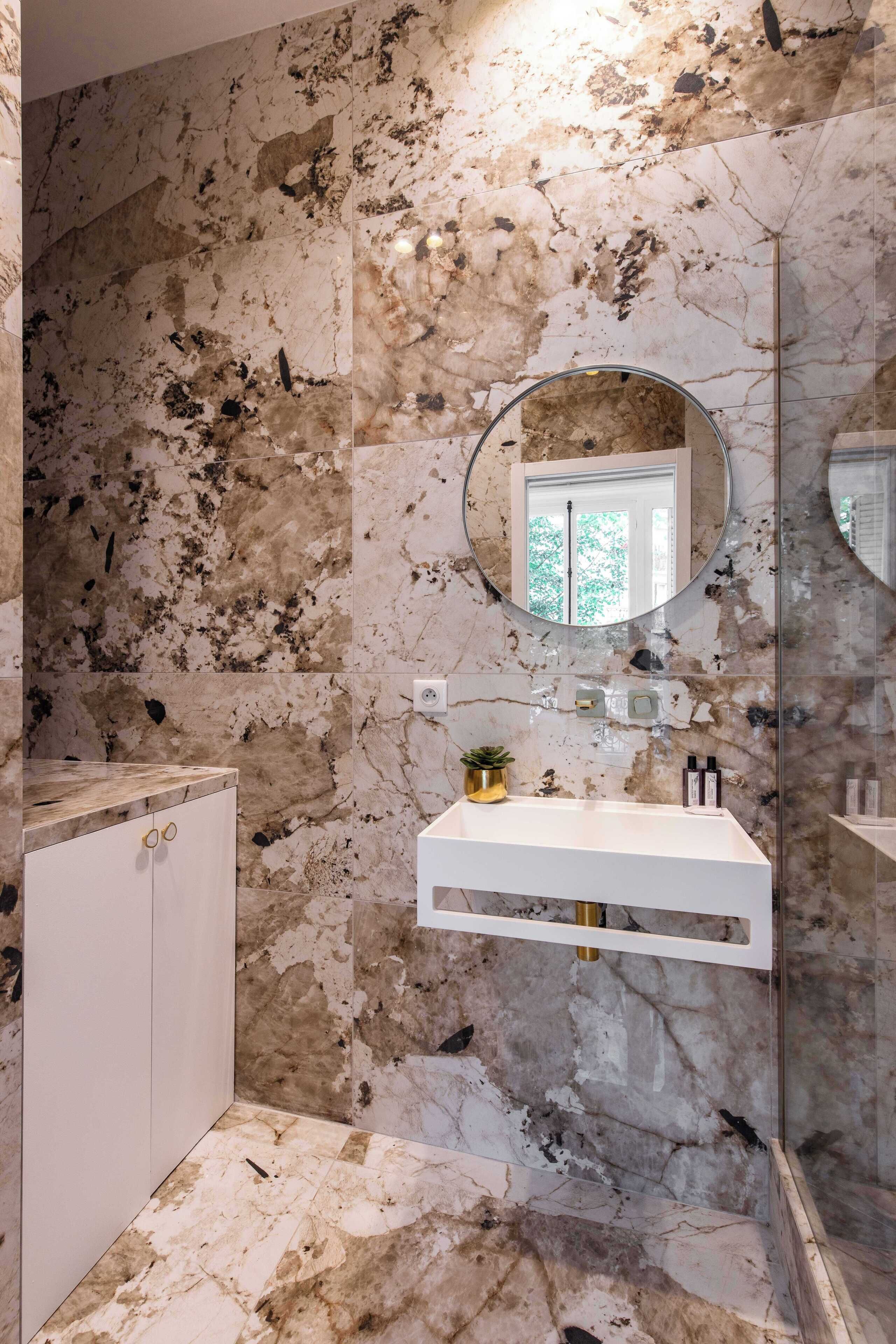 A bathroom with a marble wall, a round mirror, a white sink, and a cabinet.