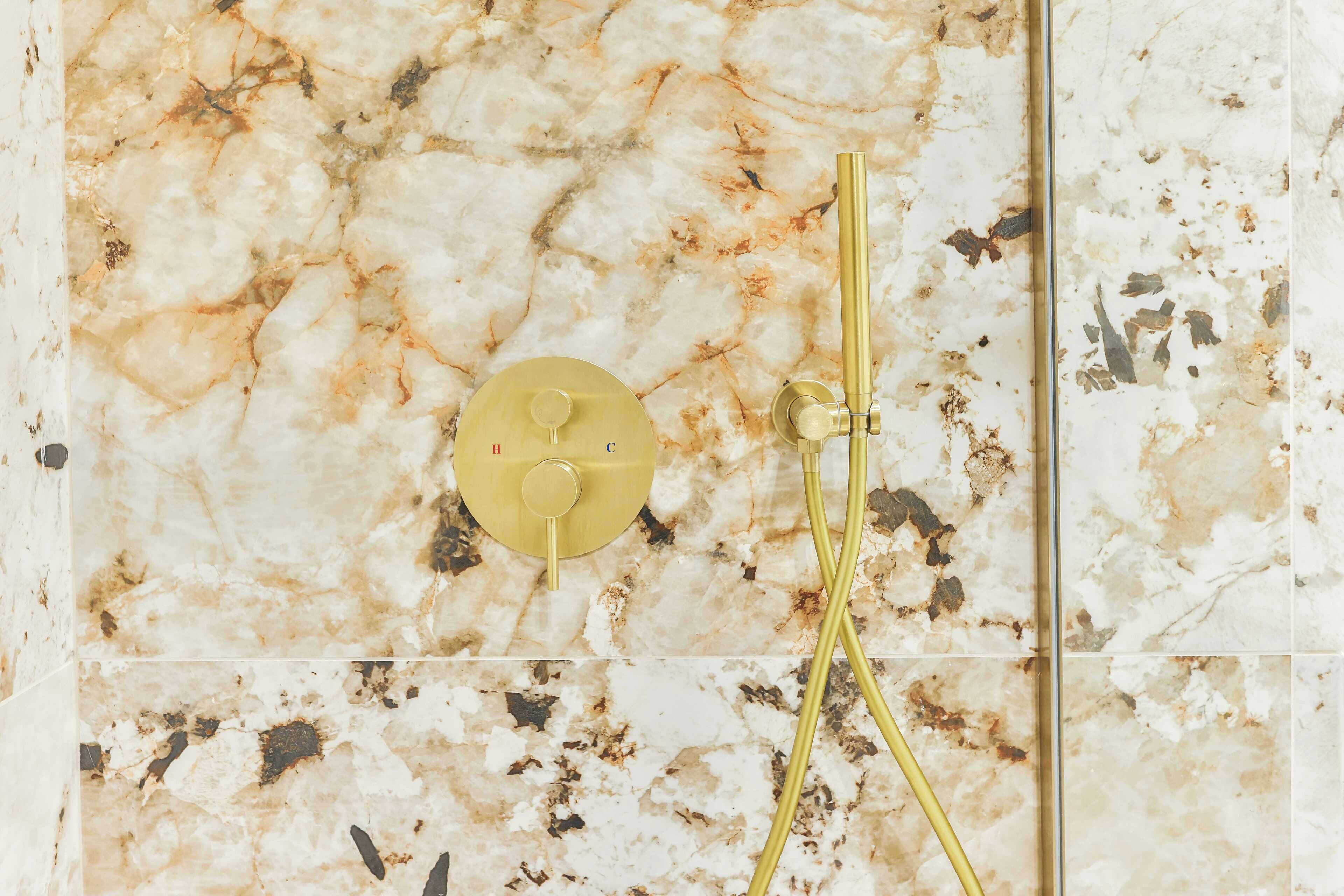 Ein Badezimmer mit Marmorwand und goldfarbener Duscharmatur.