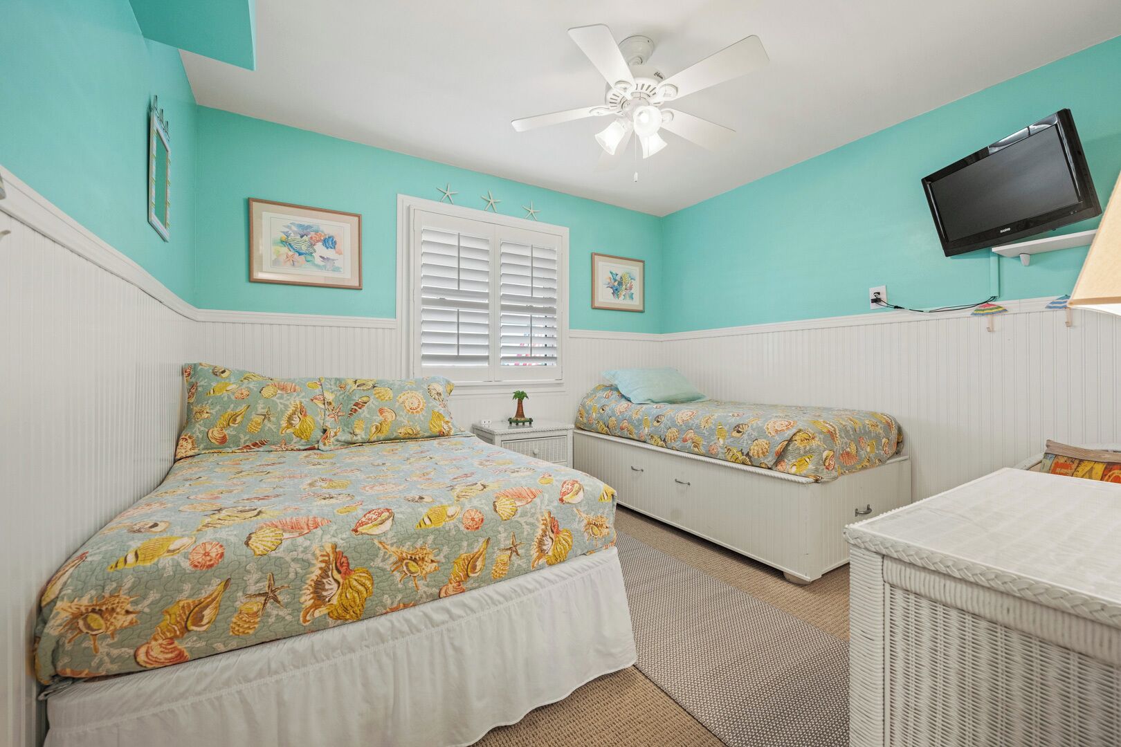 A bedroom with two beds, a ceiling fan, a TV, and a small table.