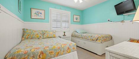 A bedroom with two beds, a ceiling fan, a TV, and a small table.