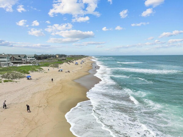 A beach with a sandy shore, ocean waves, and buildings in the background.