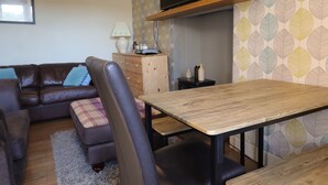 Ein Wohnzimmer mit einem braunen Ledersofa, einem Holztisch und einem Fernseher auf einer Holzablage.