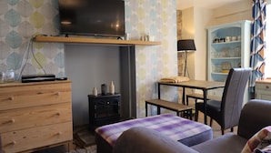 Ein gemütliches Wohnzimmer mit an der Wand befestigtem Fernseher, Kamin, Esstisch mit Stühlen und Bücherregal.