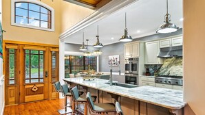 A modern kitchen with a large island, bar stools, pendant lights, and a view of the outdoors. - Luxury Smokies Home with Backyard Paradise (Sevierville)