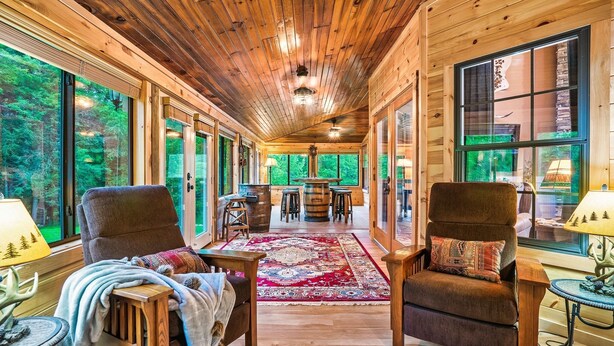A wooden interior with large windows, a central rug, and two armchairs. - Luxury Smokies Home with Backyard Paradise (Sevierville)