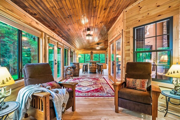 Ein Holzinterieur mit großen Fenstern, einem zentralen Teppich und zwei Sesseln.
