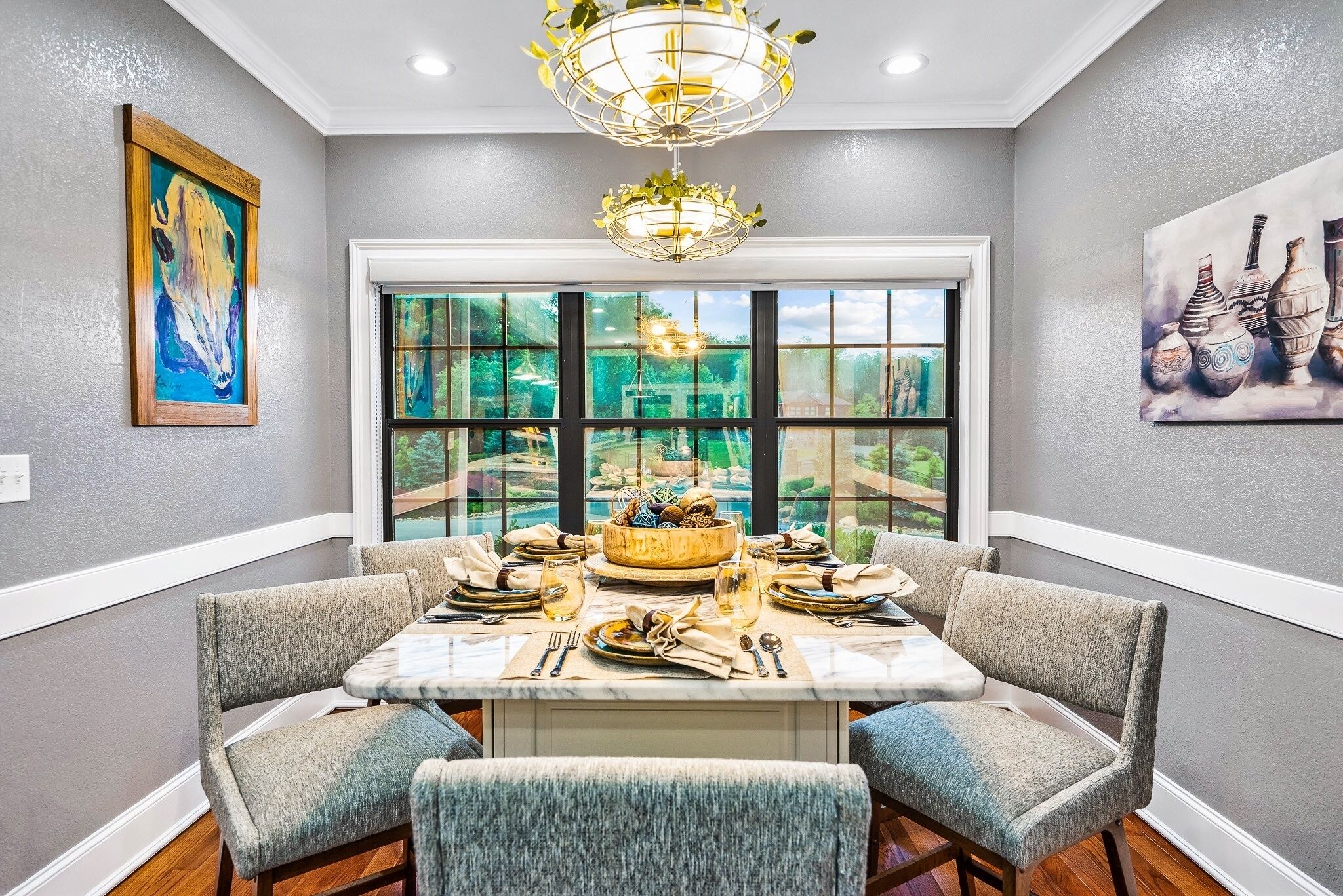 A dining area with a large window, a chandelier, and artwork on the walls.