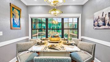 A dining area with a large window, a chandelier, and artwork on the walls.